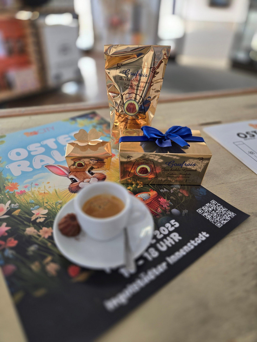 Goufrais Pralinen in goldener Verpackung, Tasse Kaffee, Osterplakat mit Hase, Geschenkschachtel