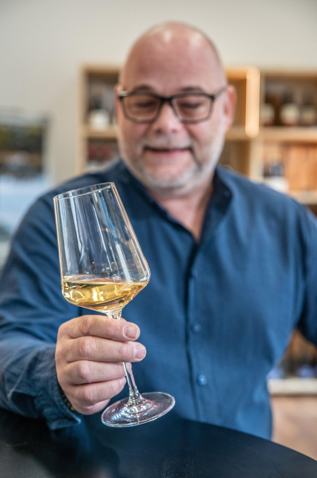 Mann mit Brille hält Weißweinglas in moderner Küche, Weinverkostung, Weinliebhaber