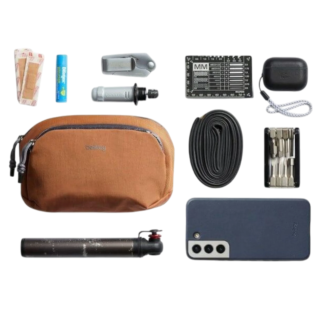 Bellroy Venture Pouch Organizer in Braun, umgeben von Zubehör wie Smartphone, Geld, Werkzeug und Schlauch.